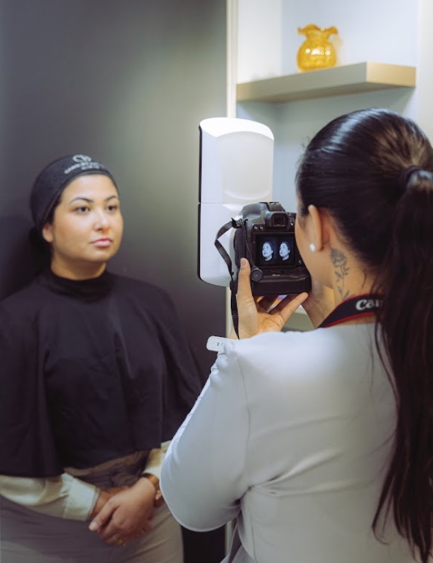 Sessão de captura com o Vectra H2 na clínica: a paciente de faixa no cabelo posiciona o rosto enquanto a equipe fotografa